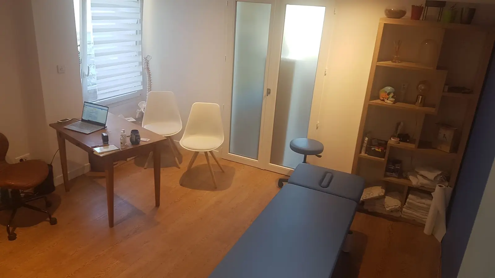 La salle de consultation, table bleue, parquet, étagères en bois et squelette de colonne près de la fenêtre
